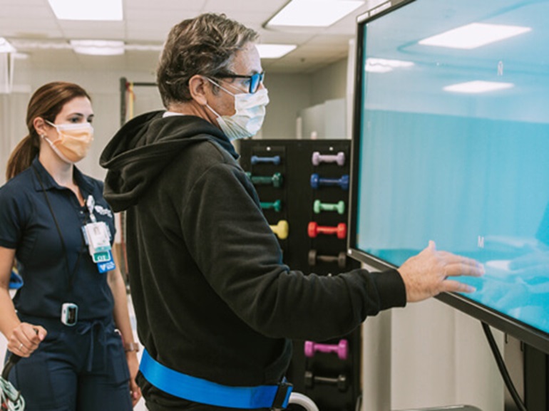 Male patient standing in front of large touchscreen monitor tracing pattern with fingertips.