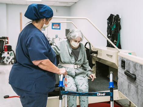 Therapist helping older female patient move from seated position to stand with a walker.