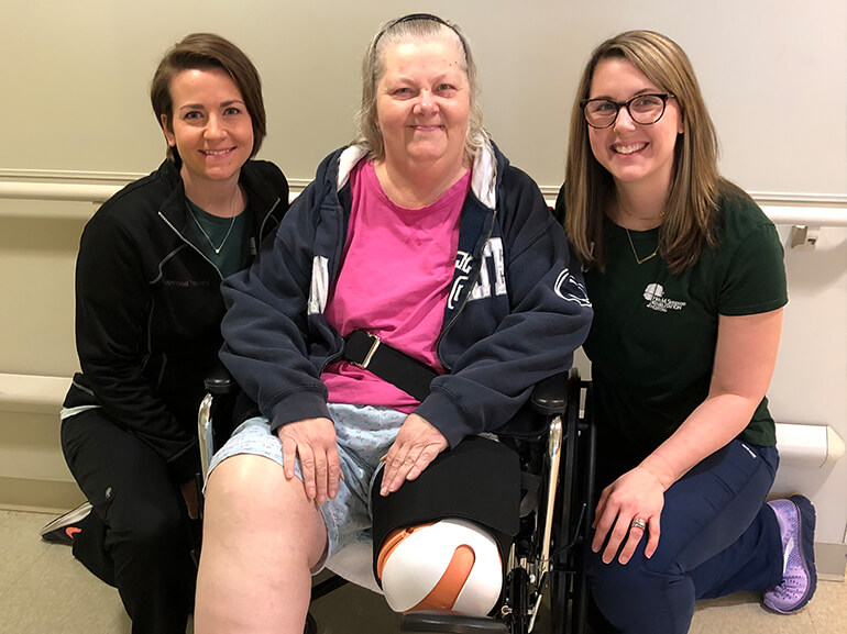 Amputee patient Vickie Joseph sitting in wheelchair beside two therapists.