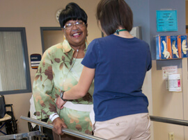 Female therapist fits a safety belt around waist of female patient.