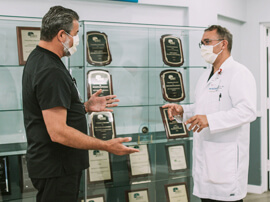 Two male doctors standing in front of awards display case talking.