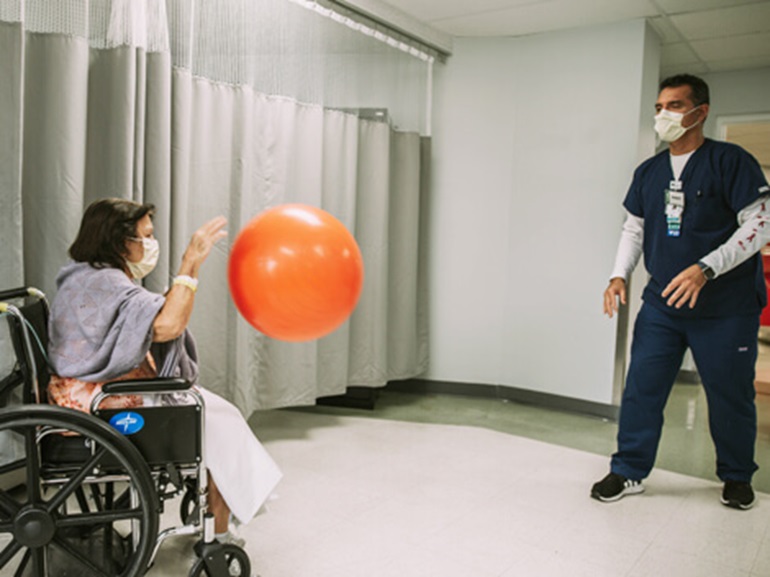 Female patient in wheelchair bouncing large orange ball back to a therapist.
