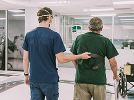 Male therapist holding on to safety harness worn by patient using a walker.