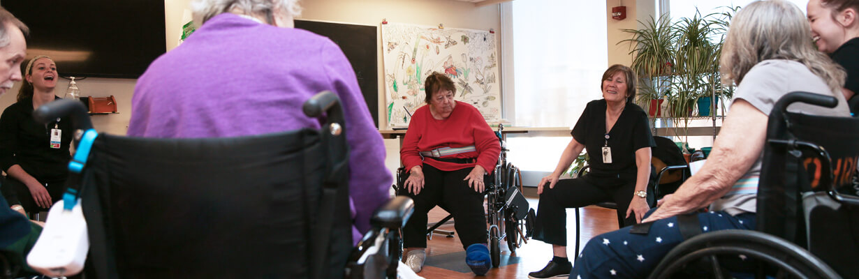 A group of patients in wheelchairs and therapists sitting in a circle in a sunny room.