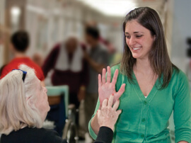 Young woman in green dress raising hand to say hello to older woman.